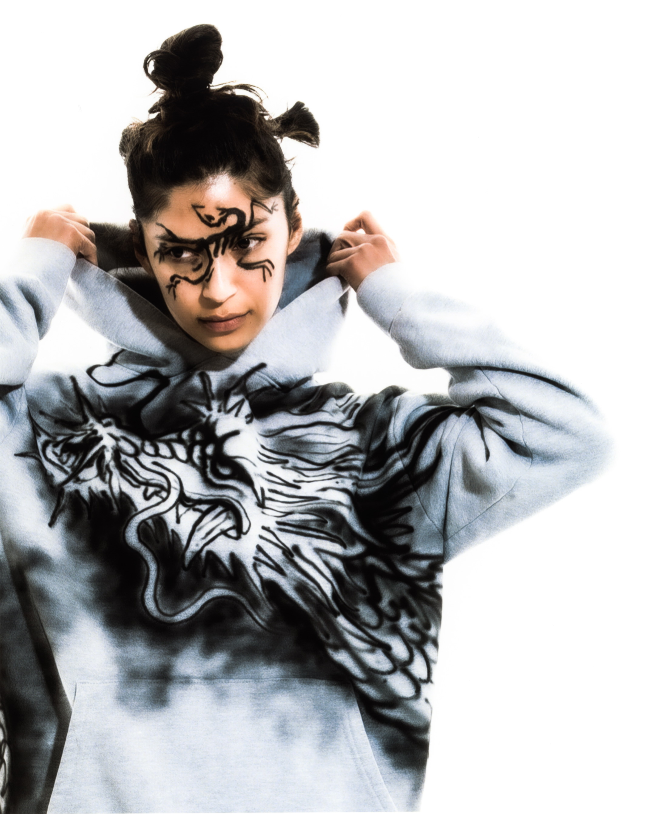 Close up shot of a model wearing black graphic liner and a gray hood with a dragon graphic on it against a white background